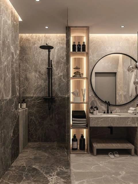 Stone shower beside an illuminated niche and a round vanity mirror