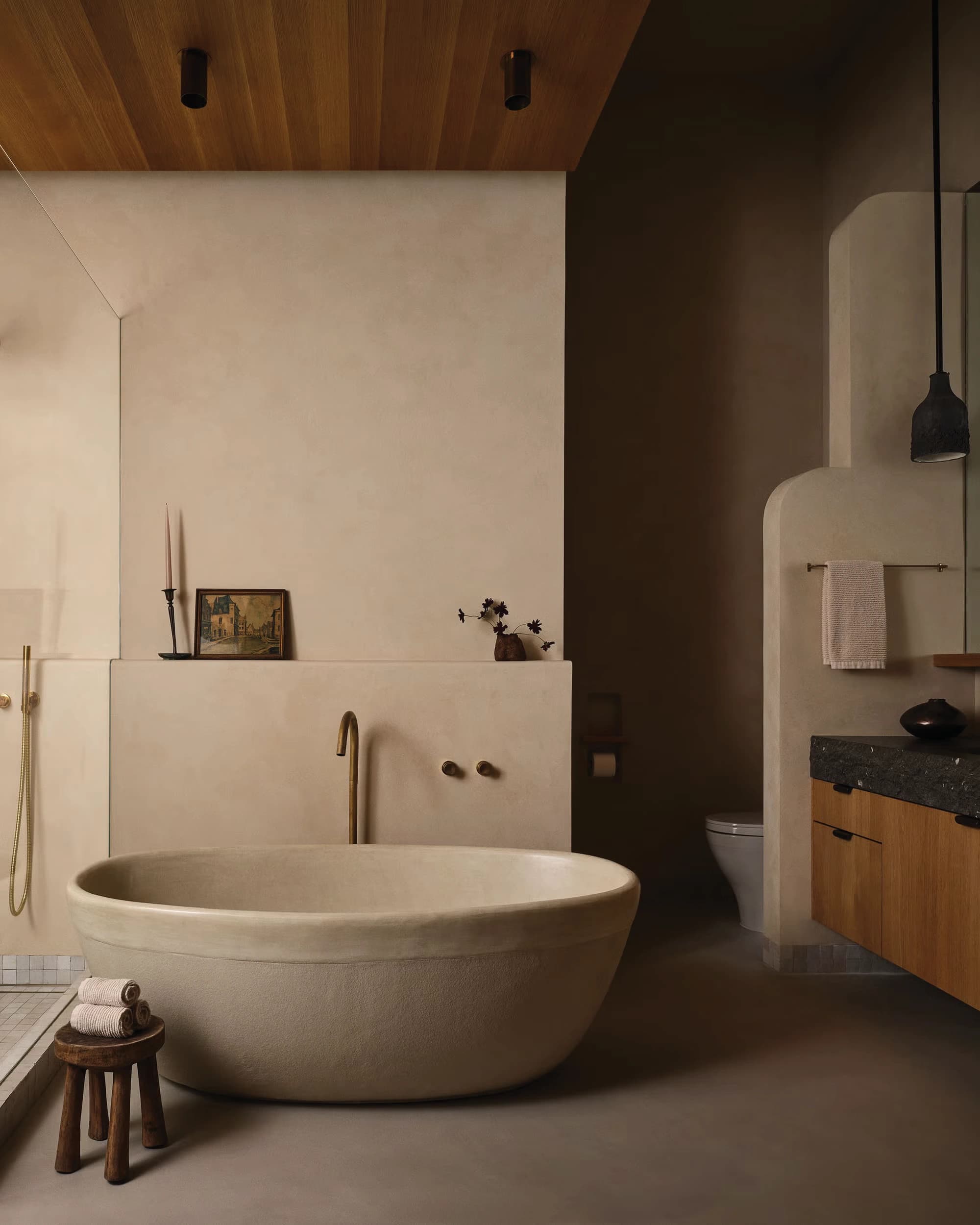 Sculptural stone bathtub with warm plaster walls and a timber ceiling